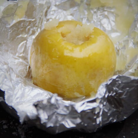 Fully baked apple resting on peeled back foil with stuffing peeking out the top.