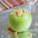 Green apple sitting on foil with brown sugar stuffing spilling out the top.