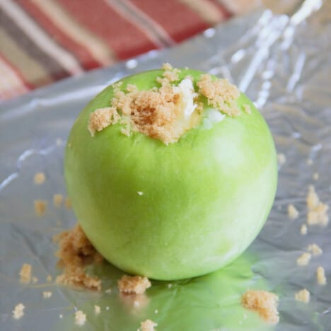 Green apple sitting on foil with brown sugar stuffing spilling out the top.