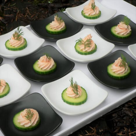 Looking down on small black and white plates with a cucumber slice and piped salmon mousse garnished with dill.