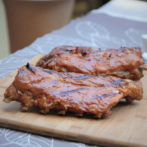 Two finished sections of ribs covered in glaze with grill marks sitting on a wooden chopping board.