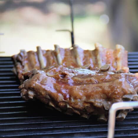 Rack of ribs covered in barbecue glazing sauce cooking on a grill.