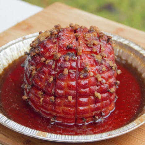 Glazed ham studded with cloves sitting in apple cider in a pie pan, ready to transfer to a board and rest before serving.