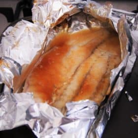 Fish filet resting in open foil pouch with wine, chilli sauce and butter, ready to cook.