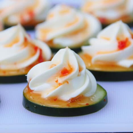 Close up of a cucumber slice topped with chili sauce dripping down a piped cream cheese swirl.