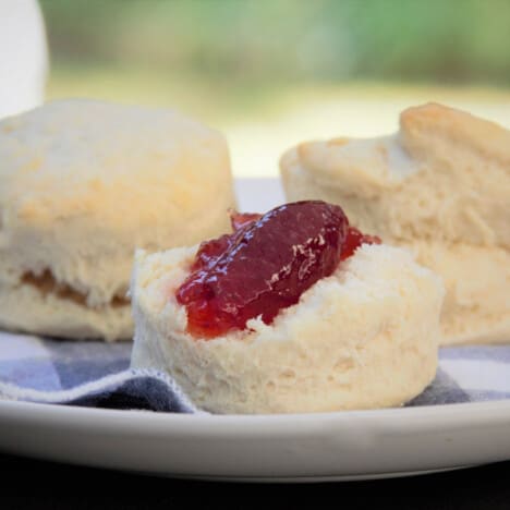 Scones being served with jam on a white plate with a blue checkered napkin.