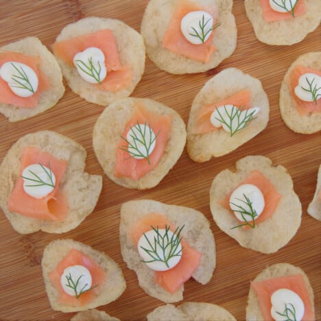 Overhead view of potato chips each topped with a small slice of smoked salmon, piped cream cheese, and a tiny sprig of dill.