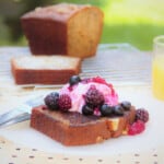 Slice of fried banana bread topped with a scoop of yogurt and mixed berries resting on a white plate.