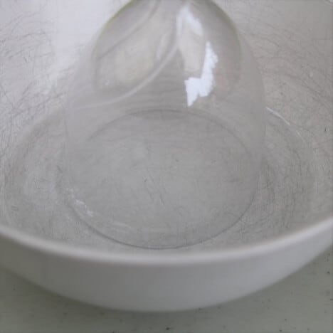 A plastic glass is being dipped in a white bowl of water.