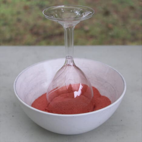 A plastic glass is being dipped into undissolved jello crystals to create a rim.