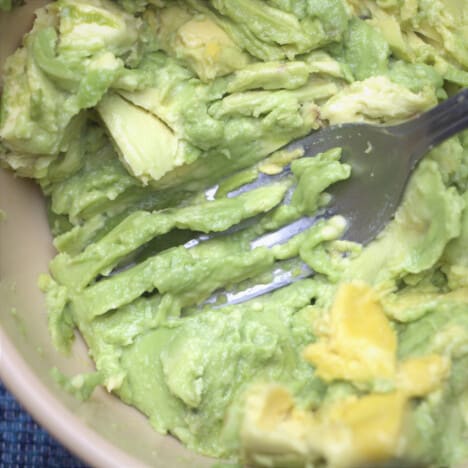 A fork mashing avocados in a bowl.