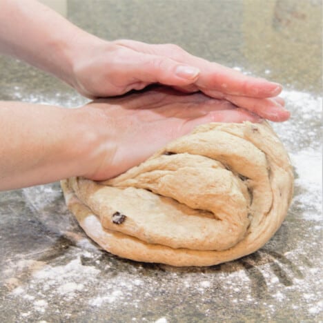 Person's hands kneading hot cross bun dough on lightly floured surface.