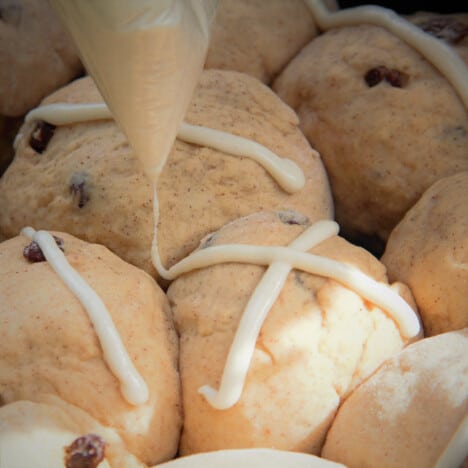 Close up of shaped hot cross bun dough balls nestled together with crosses being piped on before baking.