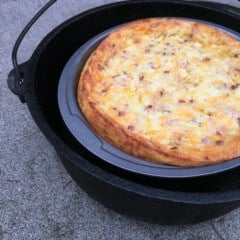 A fully baked, golden brown impossible quiche in a pie tin inside an open Dutch oven.