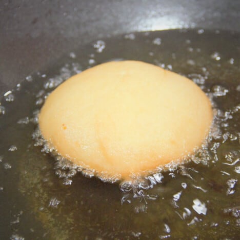 A single, golden Kitchener bun frying in hot oil.