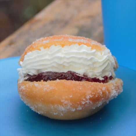 A single completed, golden brown Kitchener bun crusted with sugar and filled with piped pastry cream atop jam.