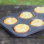A muffin tin of cooked golden brown mini bacon and egg pies resting on a wooden table.