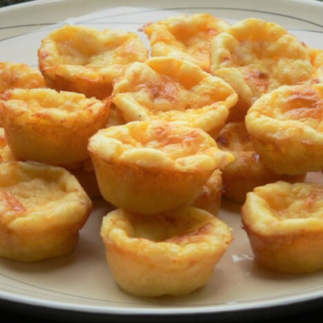 A pile of golden brown mini bacon and egg pies stacked on a plate, ready to serve.