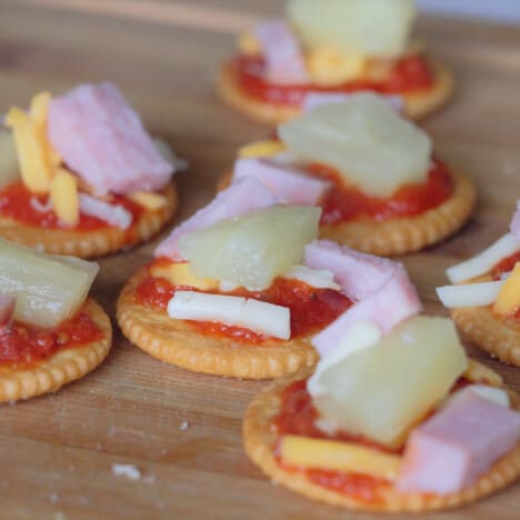 Multiple mini pizza crackers on a chopping board laid out to serve.