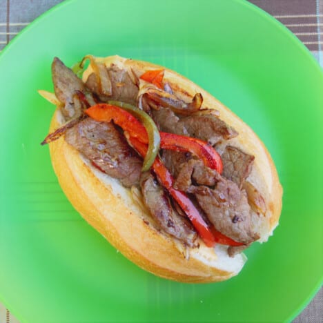 A split bread roll filled with cooked beef, onions, red and green peppers, and cheese resting on a green plate.