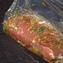 Close up of a pork tenderloin covered in marinade in a clear plastic bag.