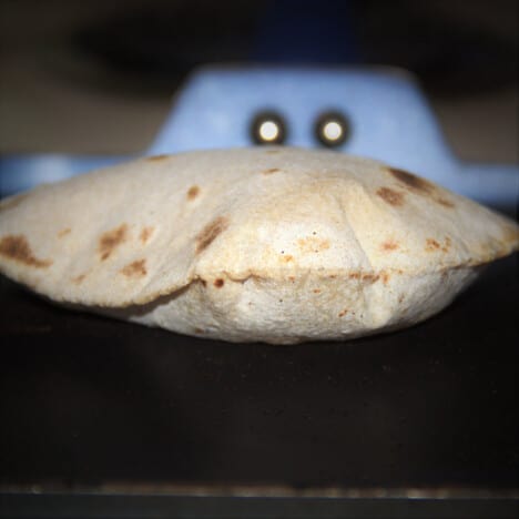 Close up of a puffed-up roti cooking on a griddle.