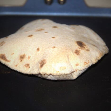 A single puffed-up roti cooking on a griddle.