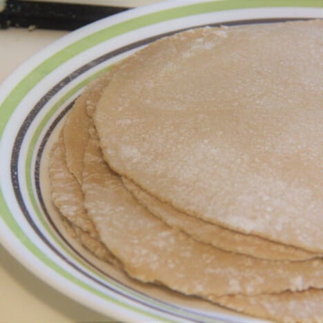 A stack of rolled-out, lightly floured roti resting on a plate ready to cook.