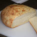 Fully baked round, domed cob loaf of bread with a browned top, loaf partially sliced to reveal an evenly baked crumb.
