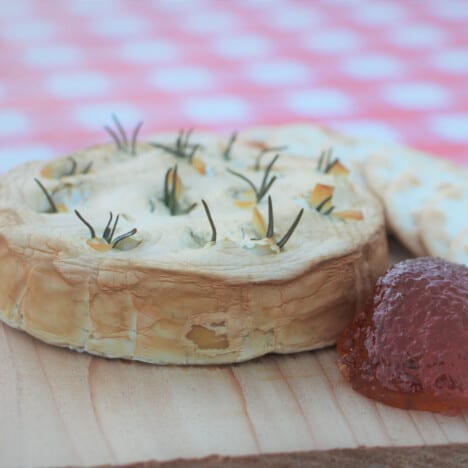 A smoked Camembert round on a wooden plank with a side of pepper jelly.