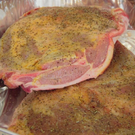 Two full pork shoulders with mustard and rub applied, resting one atop the other on foil ready to cook.