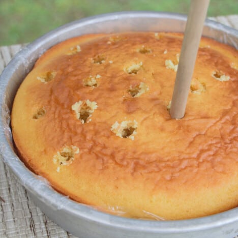 Close up of a wooden spoon poked into a baked, bare cake with a pattern of holes across the cake top.