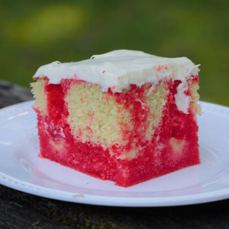 A plastic plate with a single square cut piece of strawberry poke cake topped with a white frosting.