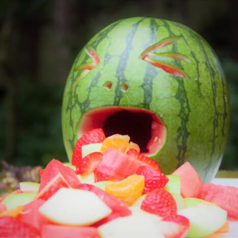 Close up of a watermelon carved to look like it is vomiting a fresh fruit salad.