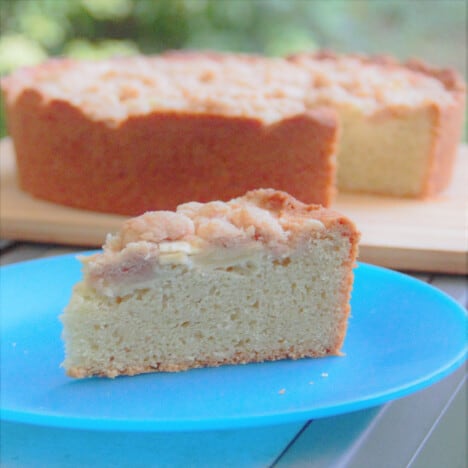 A slice of Apple Streusel Pound Cake on a blue camp plate sitting in front of the remaining cake.