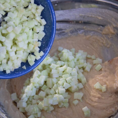 Finley diced apples are being poured from a blue bowl into the muffin batter.