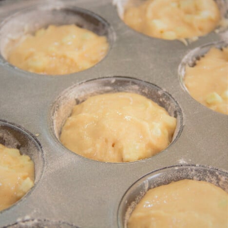 A close-up of a muffin tray with the raw apple and cinnamon batter added.