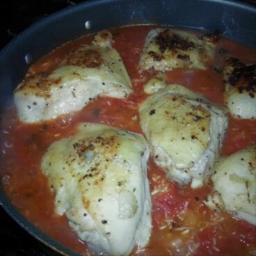 Several spiced and browned chicken breasts cooking in a Dutch oven atop the tomato sauce mixture and rice.