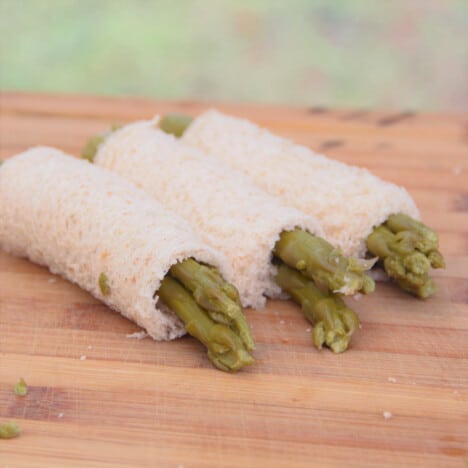 Three asparagus rolls sitting on a chopping board.