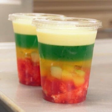 Close up of two lidded, clear plastic cups, each filled with layered trifle that’s ready to serve.