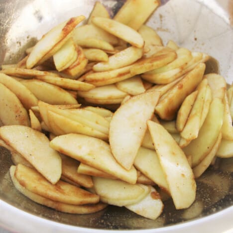 A stainless steel bowl with the prepared apple slices in their spiced and sweetened mixture.