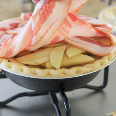 The raw bacon lattice being lifted to show the apple filling it is covering.