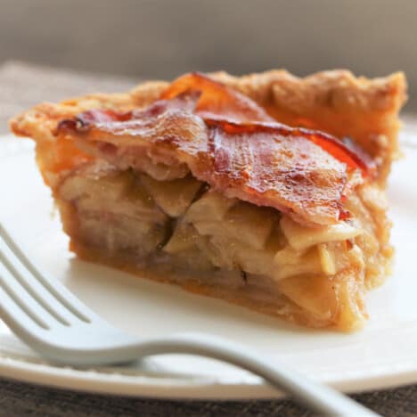 A slice of bacon-topped apple pie on a white plate with a fork.
