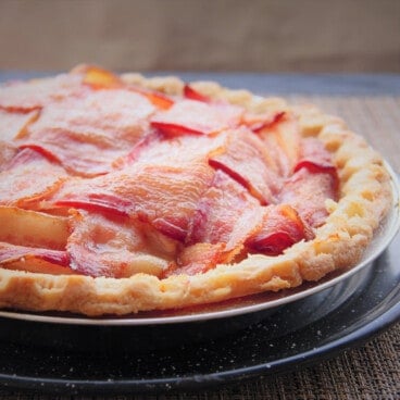 A fully cooked bacon lattice topped apple pie in a foil pie tray.