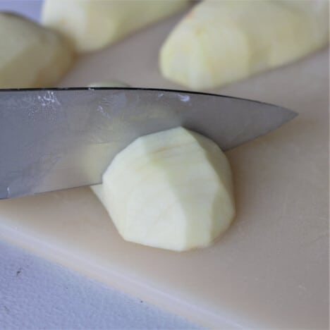 Peeled potato on a chopping board with the hasselback slits being cut into it.