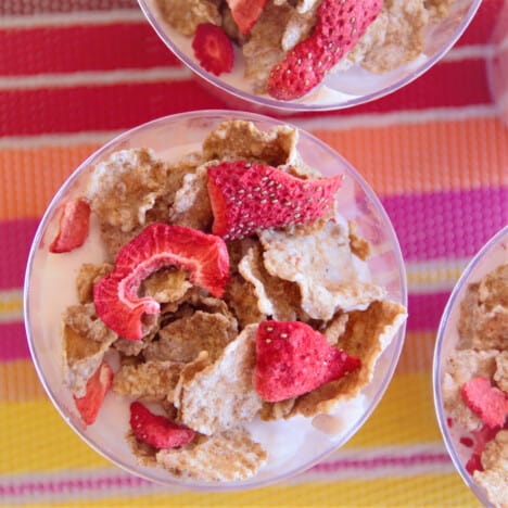 Overhead view of three breakfast parfait cups, each topped with strawberry cereal.