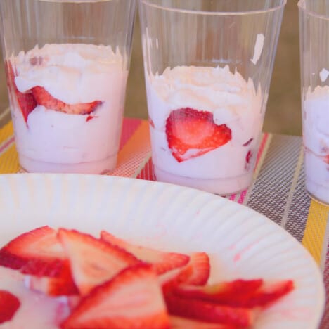 The fresh strawberry slices sitting in front of three partly constructed parfaits.