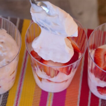 A large spoonful of strawberry yogurt being added to a breakfast parfait.