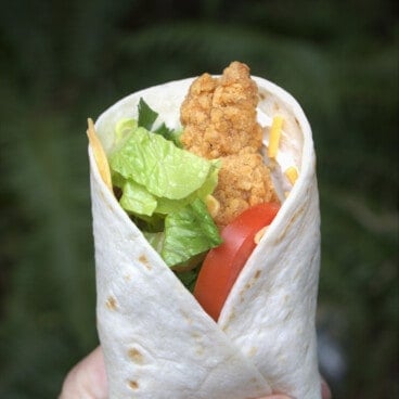 Holding up a made wrap with the fillings of the chicken nugget, lettuce, and tomato being exposed.