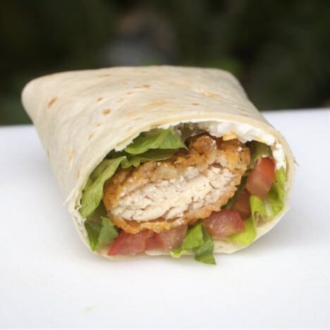 A chicken nugget wrap cup in half on a chopping board exposing the contents inside.